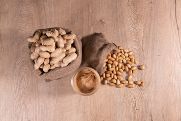 Peanut butter in glass with raw peanuts and poured roasted peanuts, top view photo