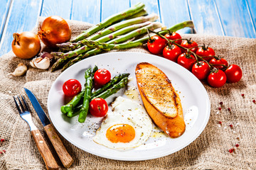 Fried egg with vegetables and toast on wooden table