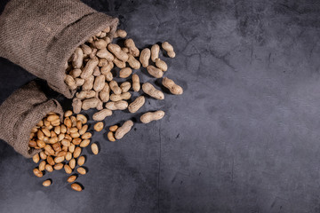 Top view photo of poured peanuts, peanuts in sack bag, aligned left for copy text, background is black stone