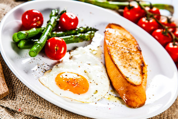 Fried egg with vegetables and toast on wooden table