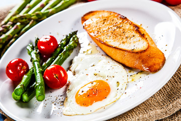 Fried egg with vegetables and toast on wooden table