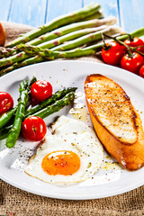 Fried egg with vegetables and toast on wooden table