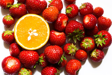Top view of half of orange surrounded by red strawberries on white background.