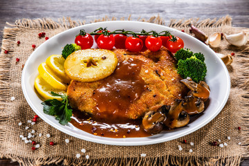 Fried pork chop with vegetables and mushrooms on wooden background