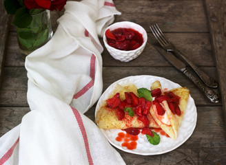 Thin pancakes with cream filling and strawberry sauce on a wooden table. Rustic style.
