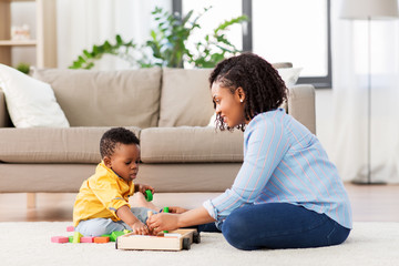 childhood, kids and people concept - happy african american mother and her baby son playing together with wooden toy blocks kit on floor at home