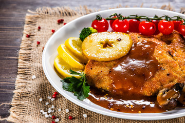 Fried pork chop with vegetables and mushrooms on wooden background
