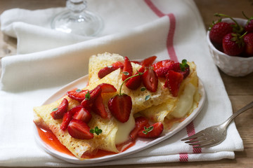 Thin pancakes with cream filling and strawberry sauce on a wooden table. Rustic style.