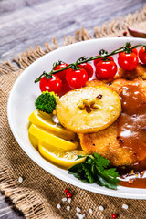 Fried pork chop with vegetables and mushrooms on wooden background
