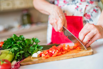 Female hand with knife chops bell pepper in kitchen. Cooking vegetables