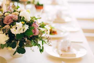 Gorgeous luxury wedding table arrangement, floral centerpiece close up. The table is served with cutlery, crockery and covered with a tablecloth. Wedding party decoration with pink and white flowers.