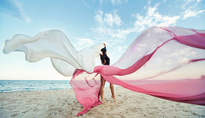 Slim Woman at the beach with long pink fabric. Sky background at the summer. Classic dancer on the...
