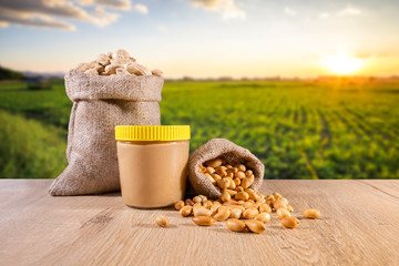 Peanut butter in glass with raw peanuts and roasted peanuts are in sack bags, background is farm