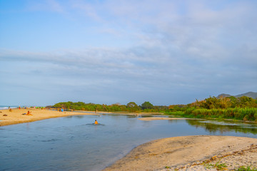A wide river flows through the tropical rainforest of South America in the delta of the sea at a beautiful sunset where people bathe and enjoy life, Colombia Palomino