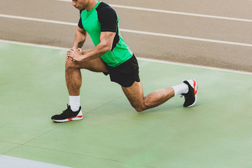 cropped view of mixed race sportsman stretching at stadium