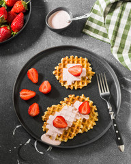 Waffles with strawberries on a black plate on a dark background