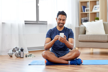 sport, technology and healthy lifestyle concept - smiling indian man with smartphone sitting on...