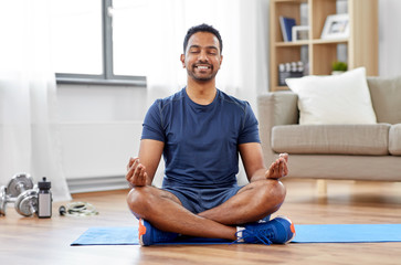 fitness, meditation and healthy lifestyle concept - indian man meditating in lotus pose on exercise...