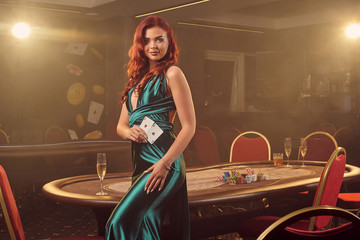 Young beautiful woman is posing against a poker table in luxury casino.