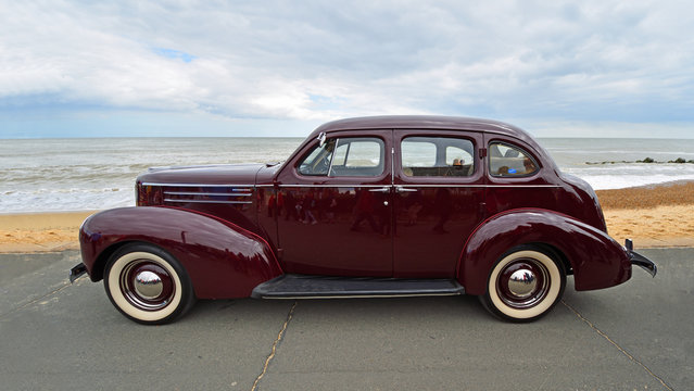  Classic Dark Red Studebaker  motor car parked  on seafront promenade beach and sea in background.