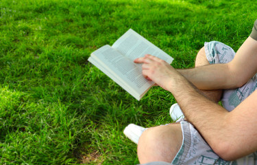 Obraz na płótnie Canvas The young man reads book on the grass field