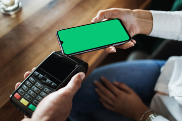 Customer making payment in modern cafe or restaurant by smartphone using NFC (near field communication) wireless technology. Close up shot. Consumer technology concept.