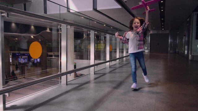 Little girl, play with a pink toy plane, running happy in the airport terminal.