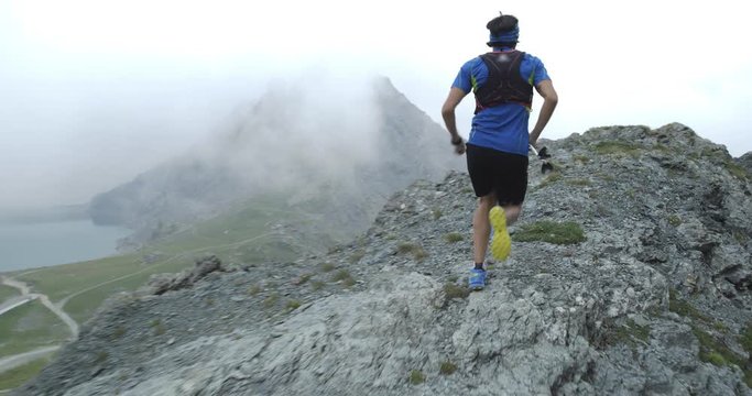 Man run on cliff edge.Trail runner running to mountain top peak training on rocky climb.Wild green nature outdoors in cloudy and foggy bad weather. Activity,sport,effort,challenge,willpower concepts