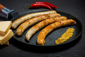 closeup frying pan with fried thin sausages, mustard, chili, and cheese