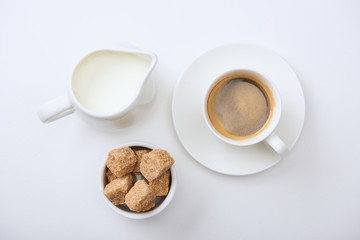 top view of tasty coffee in cup near milk and brown sugar on white background