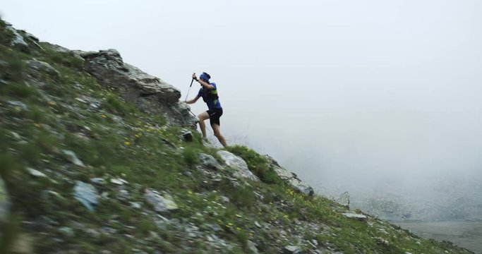 Man climbing run on mountain rise.Trail runner running to top peak training on rocky climb.Wild green nature outdoors in cloudy foggy bad weather. Activity,sport,effort,challenge,willpower concepts