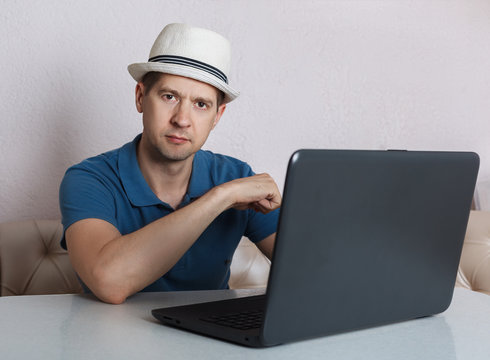 the man with the laptop sits at a table, looks in the camera
