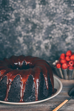 Devil's food Bundt cake covered with melted chocolate and a bowl of fresh raspberries on a table
