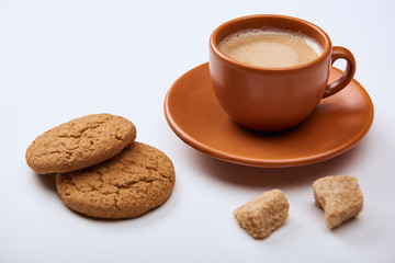 tasty coffee with foam in cup on saucer near brown sugar and sweet cookies on white background
