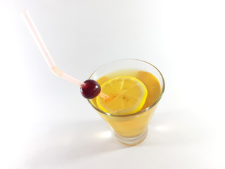 Drink with fruit in a transparent glass. Lemon and cherry for a snack. Yellow liquid in a glass. Photo
