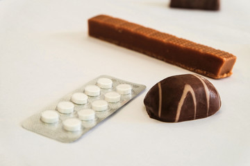 Chocolate candy and pills lie on a white table. Concept of dangerous neighborhood medicaments and sweets. Close-up. Limited depth offield.