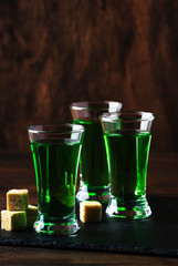 Absinthe - strong alcoholic drink, green bitter wormwood tincture in glasses on the old wooden table, place for text