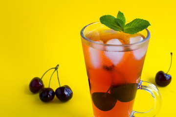 Cold lemonade with cherries in the glass on the yellow background.Copy space.Closeup.