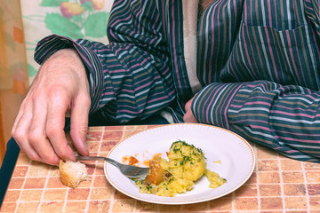 Man at the table in the kitchen eating potatoes