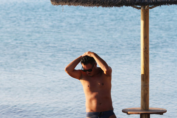 Handsome man with sunglasses and swimsuit are enjoying on the beach at sunset. Apulia, Salento, Italy