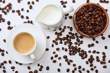 top view of coffee near scattered roasted beans, wooden bowl and milk jug