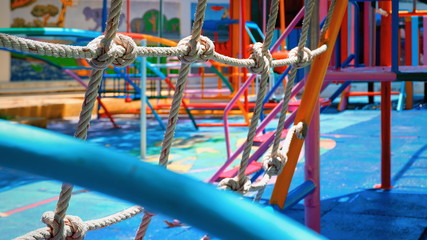 Focus on rope mesh and blurred colorful outdoor play equipments in playground area at kindergarten...