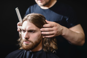 Handsome bearded man, hipster with beard and moustache has haircut in hairdressing saloon or...