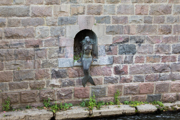Sculpture, metal statue of a mermaid sitting by the Vilnius River near the Republic Uzupis in Lithuania. Mermaid in the middle of a brick wall on the river bank.
