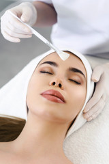 Model in white headband bandage cap lying on couch with closed eyes. Hand of beautician doctor in white glove touching her face with brush. Head and shoulders, healthcare, cosmetology, beauty clinic