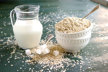Raw Oatmeal in a bowl on the table, milk in a jug, sugar and spoons. Ingredients for Breakfast.