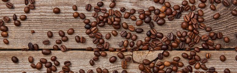 panoramic shot of wooden weathered table with scattered fresh roasted coffee beans