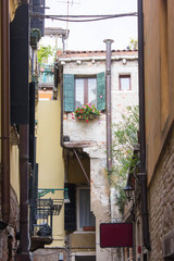 Courtyard of residential houses of the locals of Venice. Drainpipe on the facade and a balcony with flowers and shutters on the windows. Very narrow street, lane at the daytime. Non touristic place.