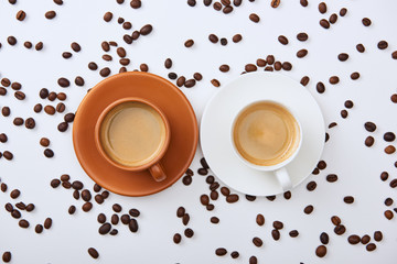 top view of coffee in white and brown cups on saucers near scattered roasted beans