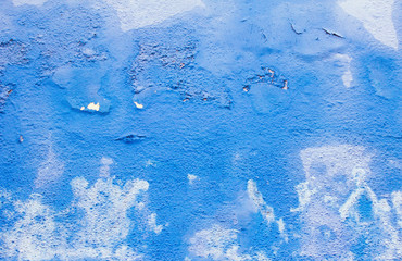 Blue wall in peeling paint. The shabby texture of the facade of a residential building painted in bright blue. White stains and spots. Blue trendy background. Aged surface of the wall in the city.